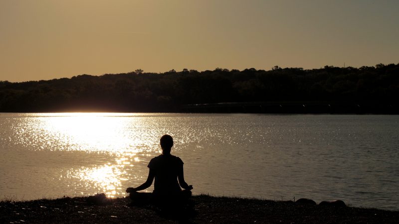 silhouetted person meditating by water