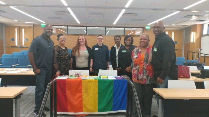 A group of people with nametags around a table draped with the rainbow flag