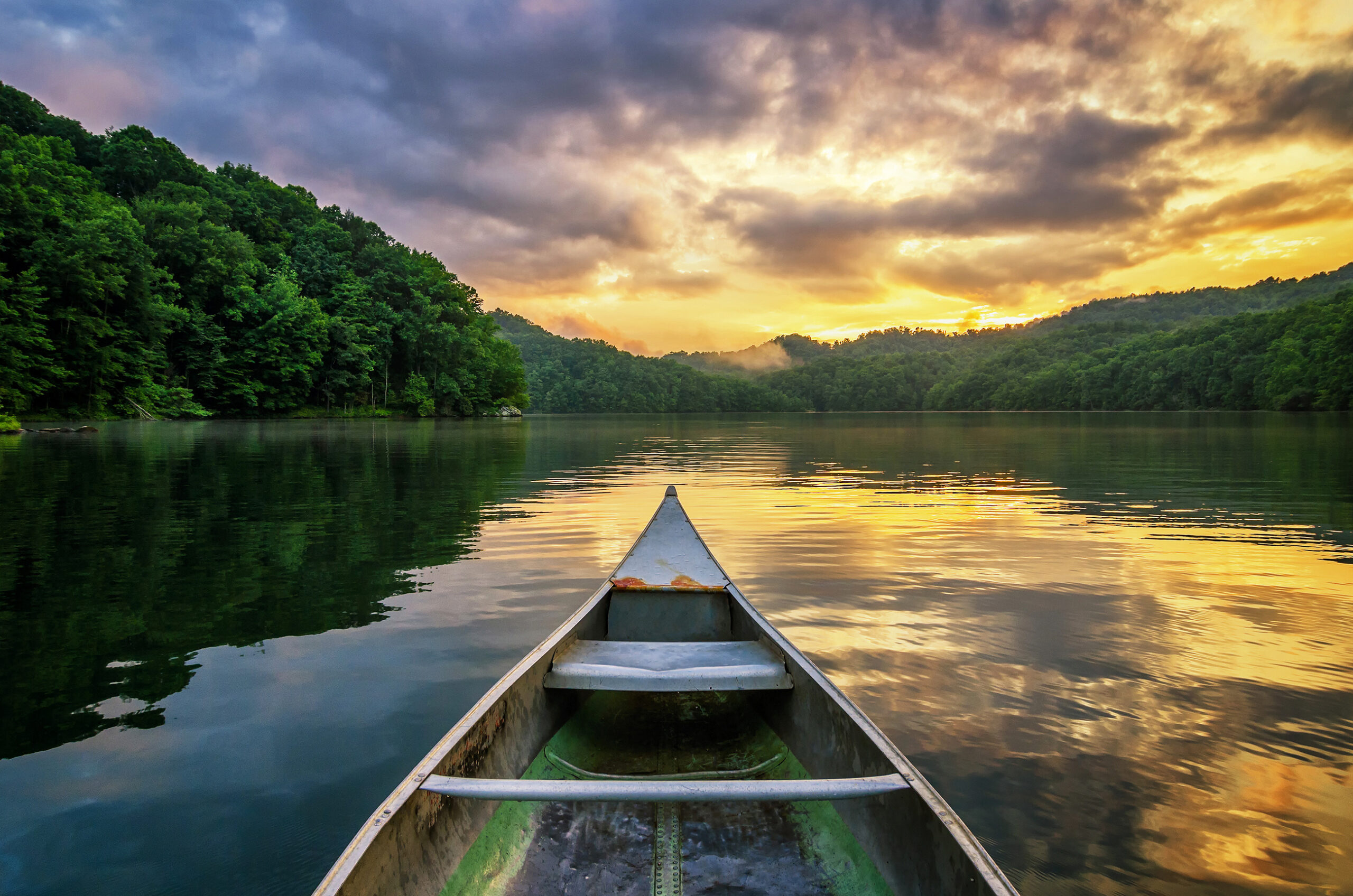 A sunset over a lake and canoe bow