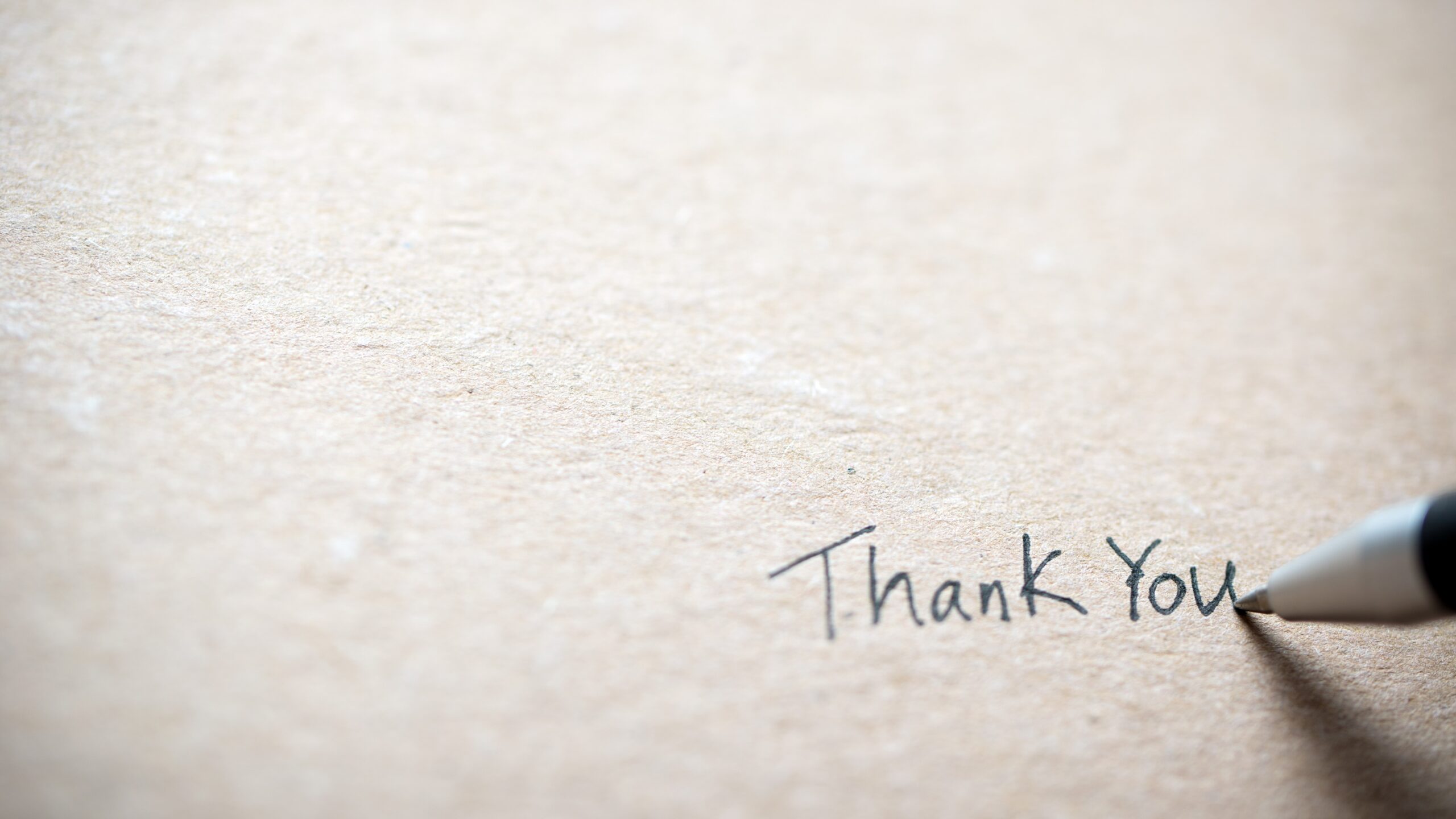 ink pen finishes a hand-written "Thank you" in the lower right corner of a piece of white paper.