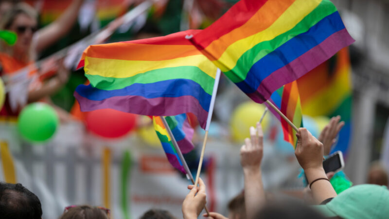 2 small, rainbow, LGBTQIA+ pride flags waving in the air